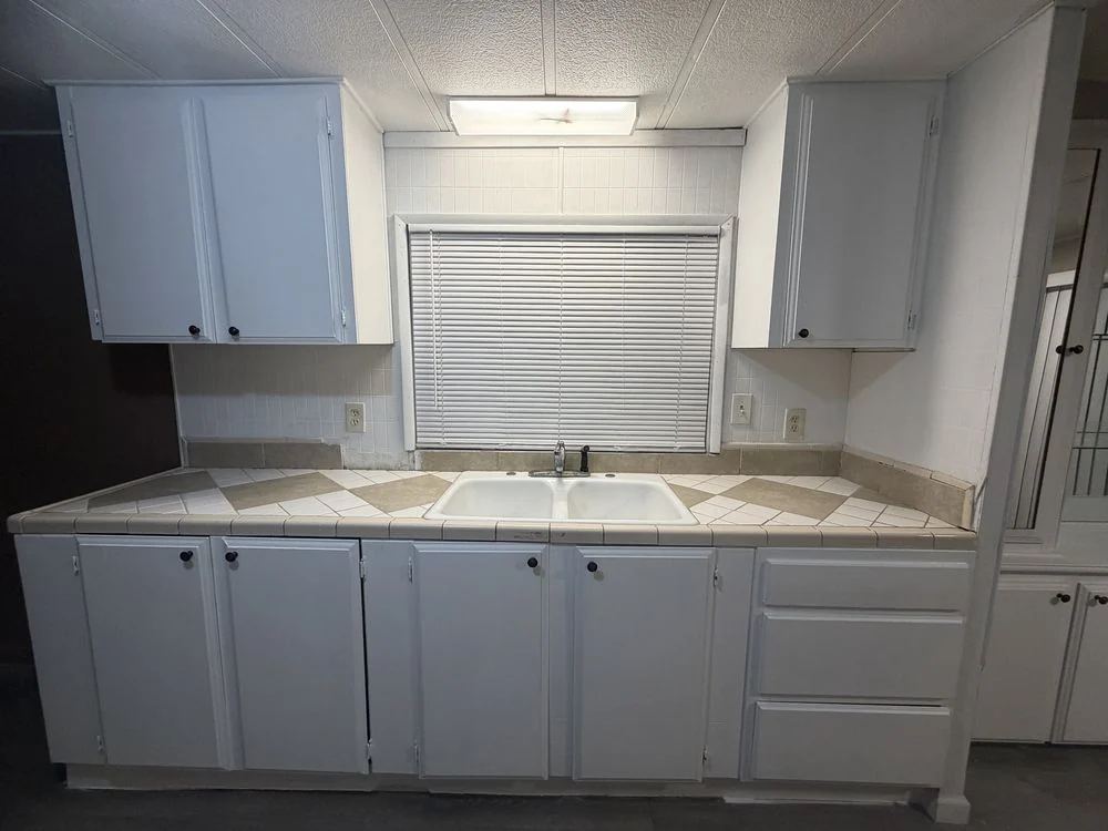 White kitchen cabinets surrounding a tiled countertop and sink